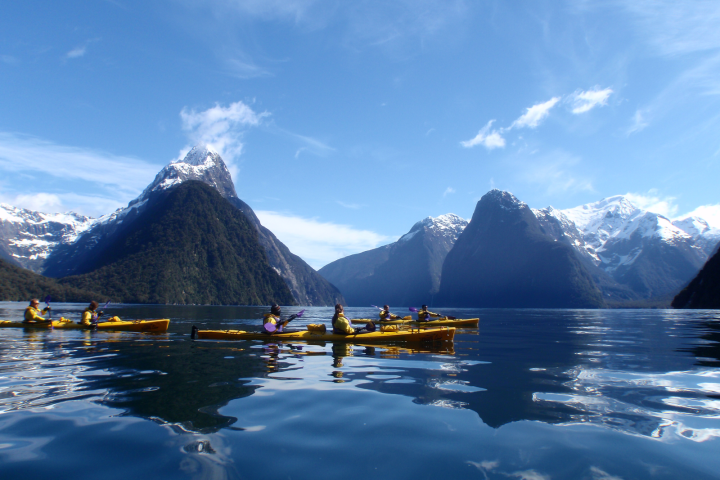 a small boat in a body of water with Milford Sound in the background